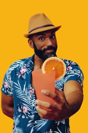 Male passing a cocktail while wearing colorful shirt with yellow background