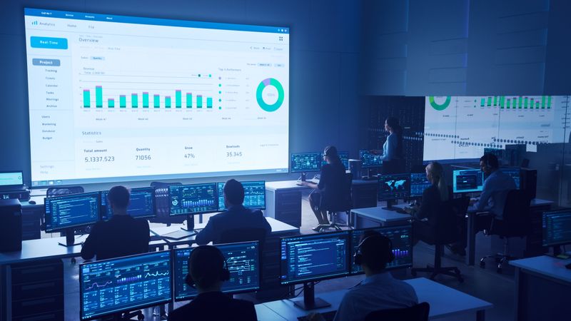 Analysts Monitor Data in Futuristic Control Room. Large Screen Displays Project Overview With Charts.