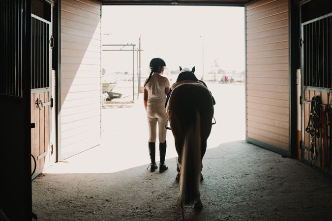Jockey leading horse out of stable