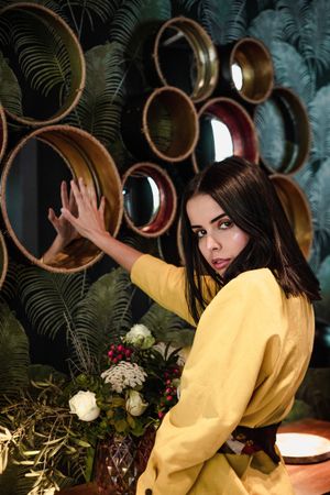 young woman in stylish clothes touching mirror near plants