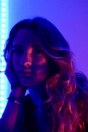 Portrait of teenage girl resting chin on hand in purple lit studio