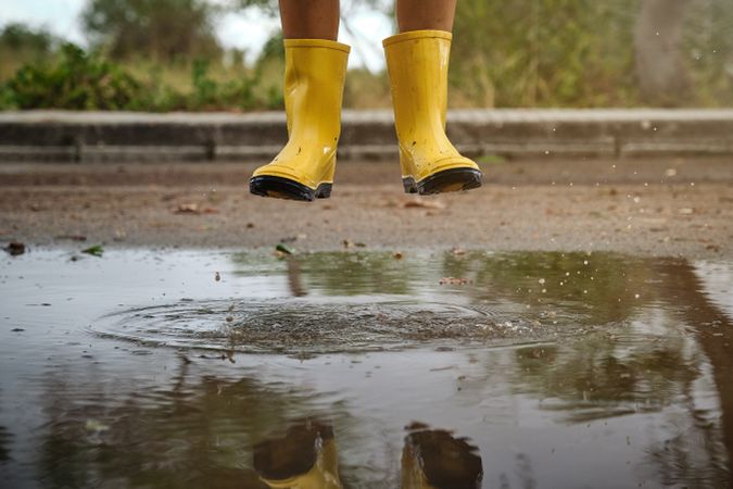 Unrecognizable kid in gumboots jumping in puddle