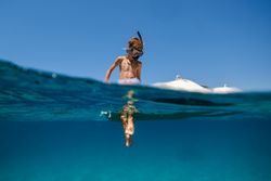 Boy in snorkeling mask floating on board of boat in sea