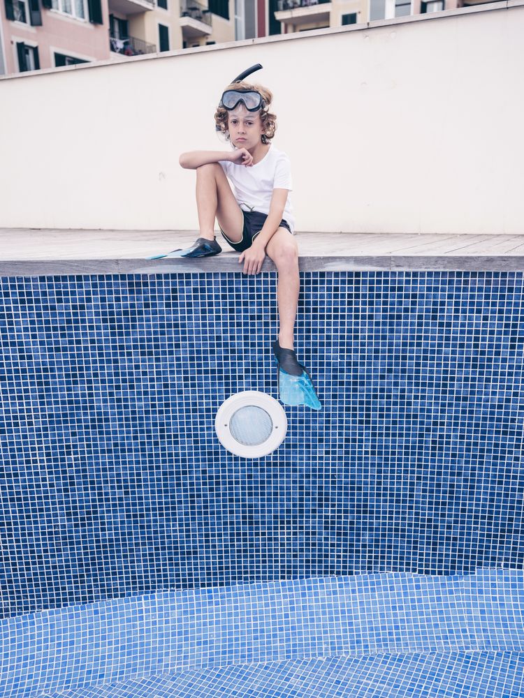 Sad preteen boy sitting on side of empty pool