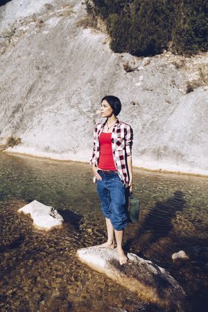 woman standing on rock with case near clear water in lake