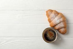 Top view cup of coffee and croissant on wooden table, copy space