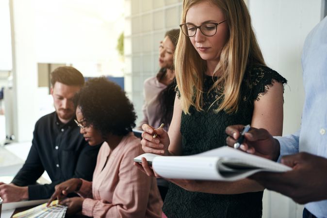 Woman taking notes at office surrounded by her colleagues