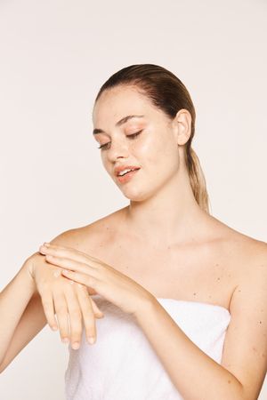 Delighted female applying recovery cream on hands