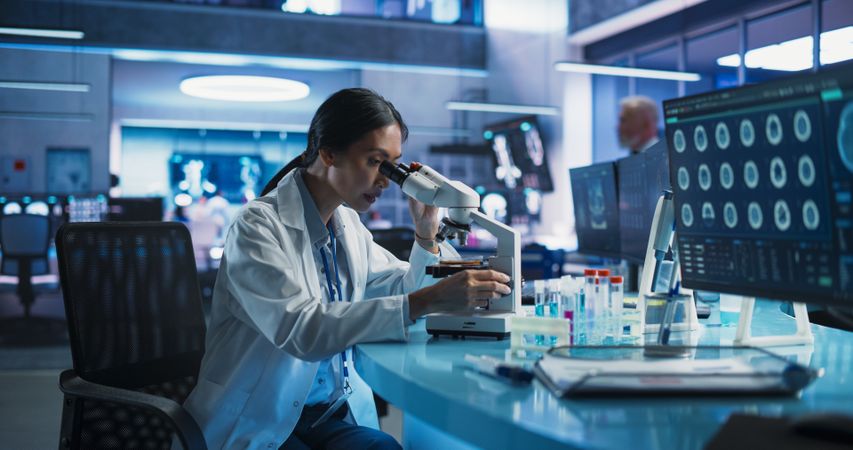 Medicine Development Laboratory: Asian Female Scientist Using Microscope, Analyzes Petri Dish Sample.