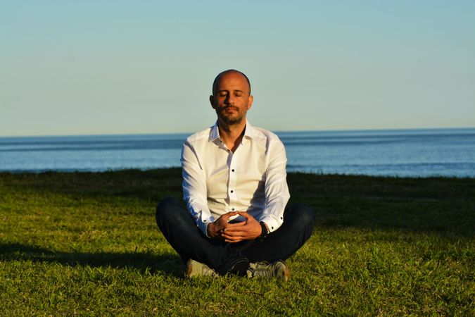 Man sitting calmly on patch of grass by the coast