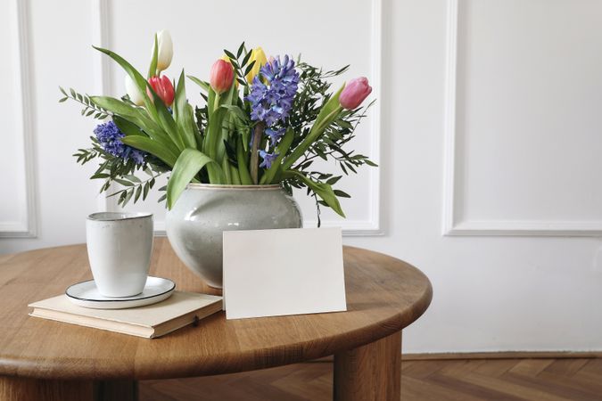 Blank card leaning on vase of flowers on table with cup of coffee