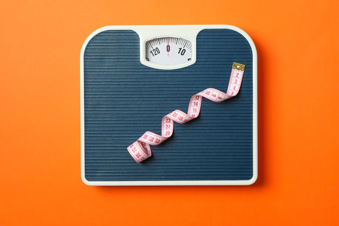 Blue weigh scales with measuring tape on orange background, top view