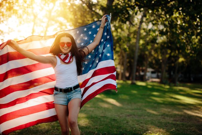 Woman in shorts running in the park holding American flag.