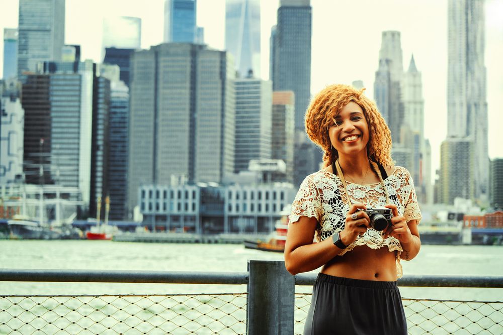 Happy Black woman photographer ready to take photos of Manhattan skyscrapers
