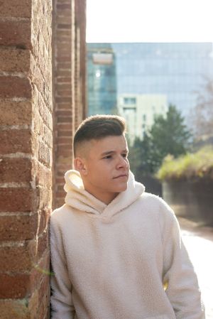 Portrait of serious young man leaning against brick wall in the sunshine