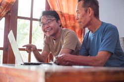 Happy adult son teaching older father using laptop