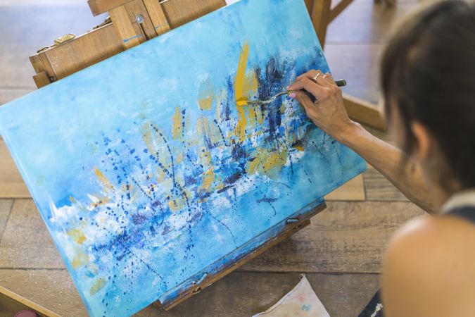 Close up of a woman painting on a canvas a blue abstract painting.