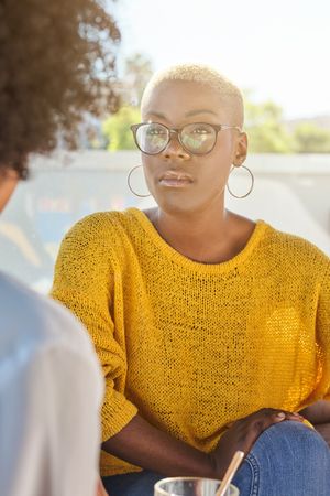 Thoughtful Black woman in yellow sweater listening to friend