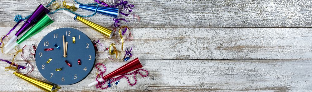 Happy New Year concept with clock nearing midnight on rustic wooden background plus party decorations