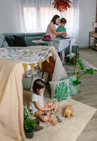 Mother teaching her teenage son to iron while her daughter play camping at home