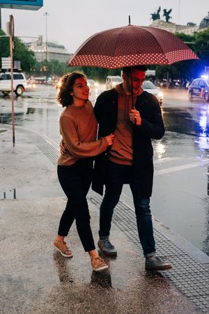 Happy couple with umbrella hugging on wet street