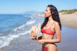 A Serene Beach Moment A Woman in a Stylish Bikini with a Straw Hat Relaxing by the Sea
