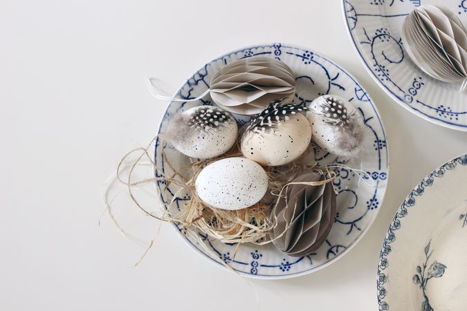 Top view of vintage blue floral plates with traditional speckled eggs with feather isolated on table