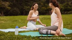 Fitness women sitting on yoga mats and relaxing during workout in a park 0Wna1b