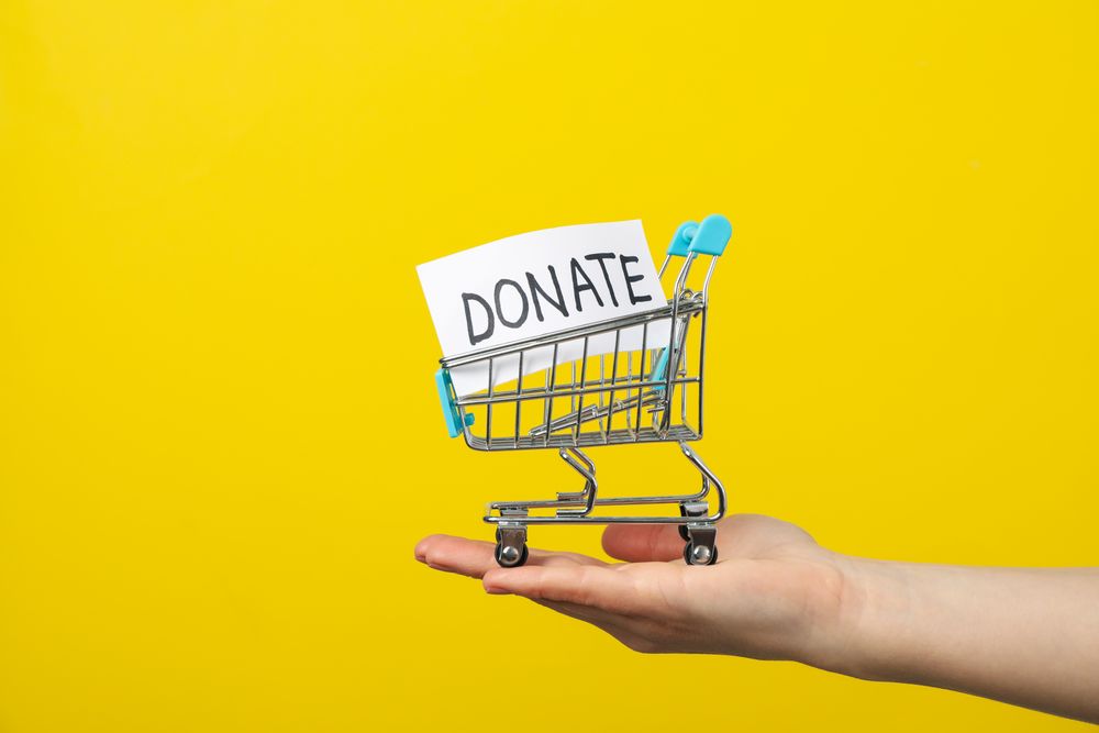 Female hand holds shop cart with text Donate on yellow background
