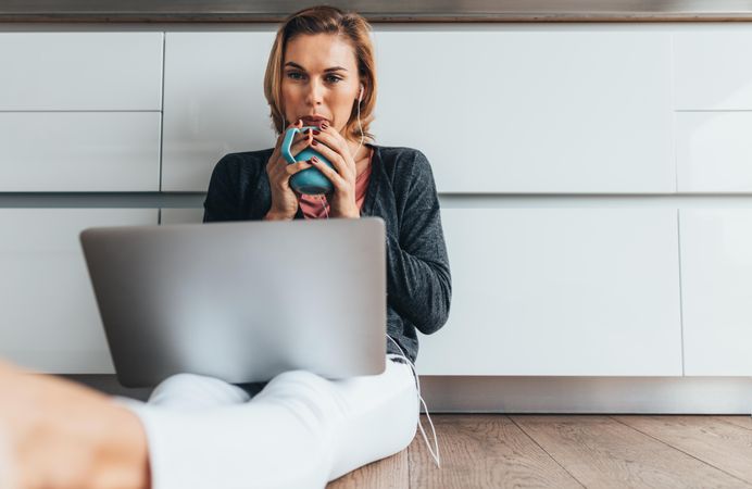Woman sitting on floor holding  a coffee mug working on laptop computer