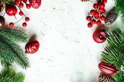 Green wintry branch with pine cones and red ornaments on bright background with copy space