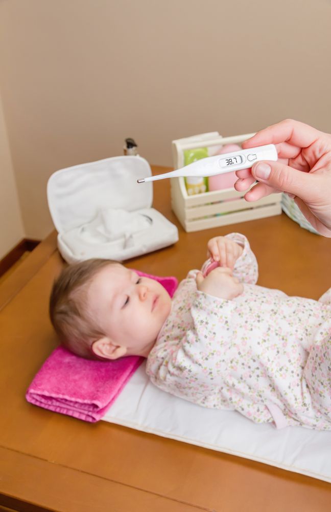 Hands holding thermometer before baby, vertical