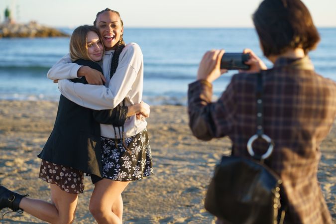 Happy girlfriends taking pictures of each other on beach at sunset