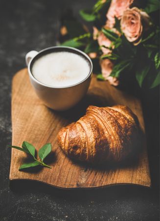 Coffee with croissants and pink roses on wooden board