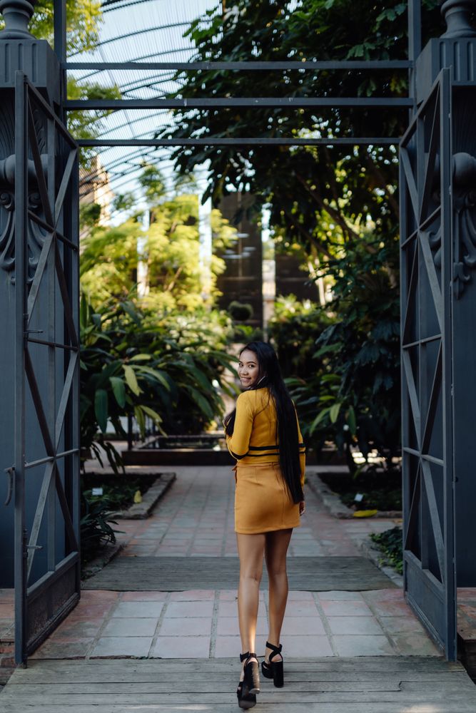Stylish long haired Asian woman walking in square under metal fence