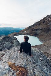 Back view of man sitting on water of frozen lake in mountain