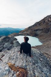 Back view of man sitting on water of frozen lake in mountain 0yGWq4