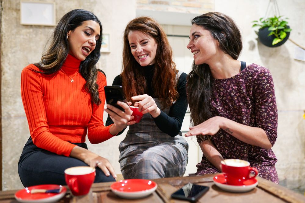 Female friends smiling at something on a friend’s smartphone