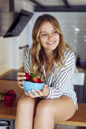 Young seductive female eating strawberry in kitchen