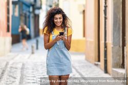 Smiling woman checking phone while strolling in front of metal door, copy space 4manB4