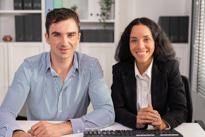 White man and Latina female colleague sitting behind desk in workplace