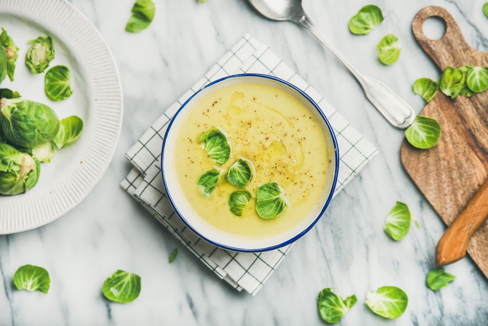 Brussels sprout soup, garnished with fresh sprouts, next to wooden board