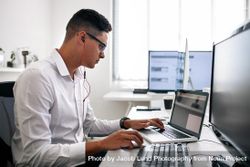 Man wearing spectacles working on laptop computer in office 0LOXAb