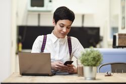 Smiling woman in loft apartment checking her smart phone while working at home
