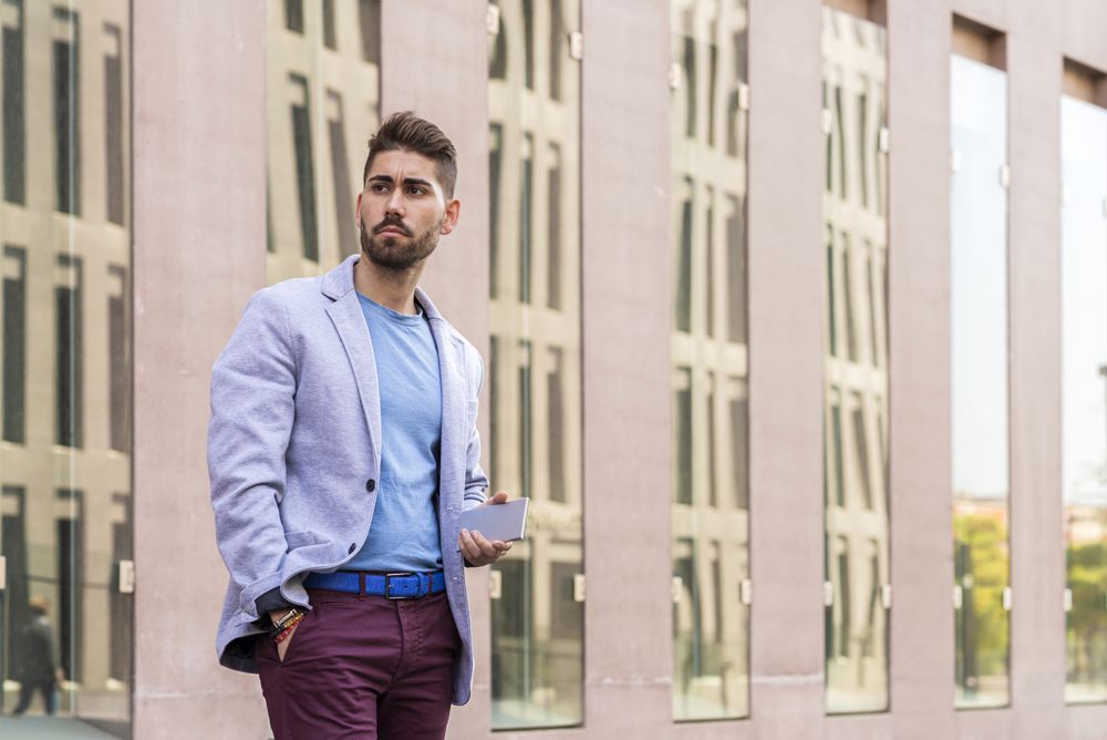 Portrait of a happy bearded young man holding a smartphone while standing outdoors and looking away