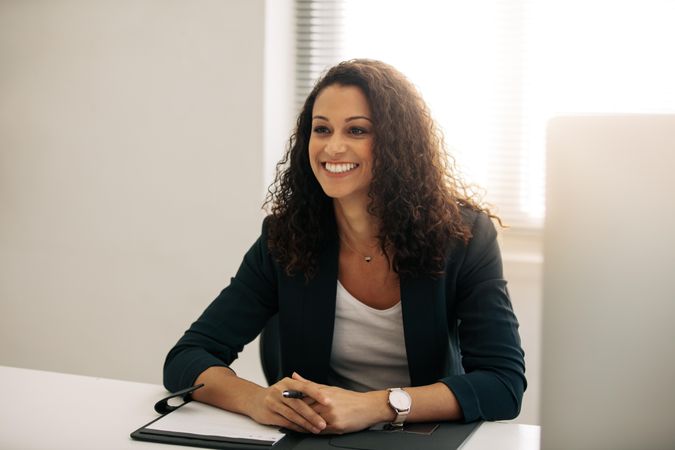 Businesswoman with curly hair in formal clothes sitting at her desk in office