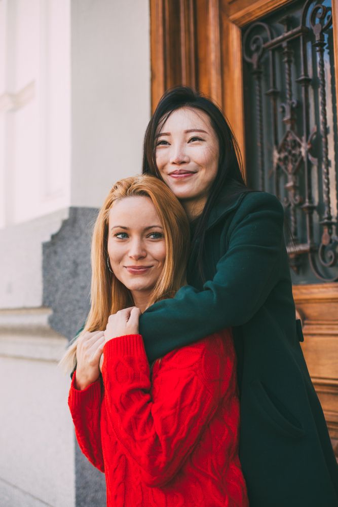Cheerful female friends hugging near ornamental door