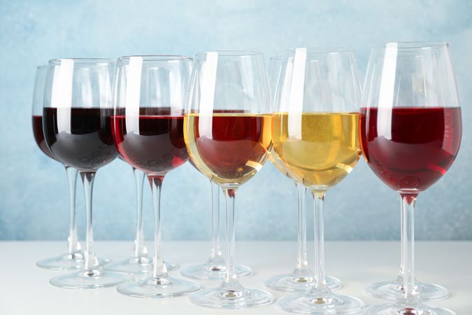 Glasses with different wine on table against light blue background