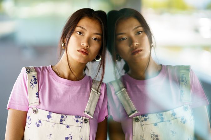 Serious female in floral overalls leaning head on window