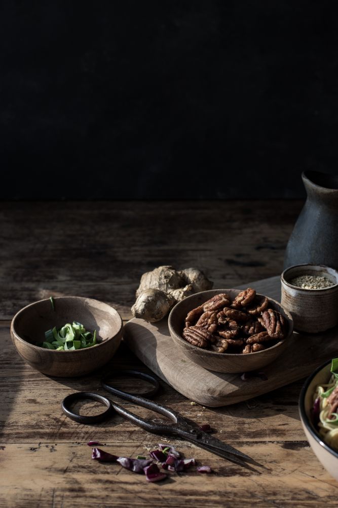 Bowl with pecan nuts near scissors, cutting board, pitcher and ginger